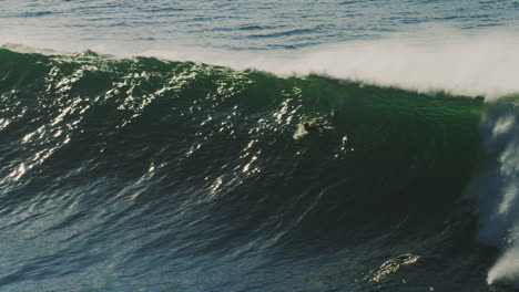 slow motion view of surfer paddling into sparkling wave as it grows into stunning monster engulfing athletes