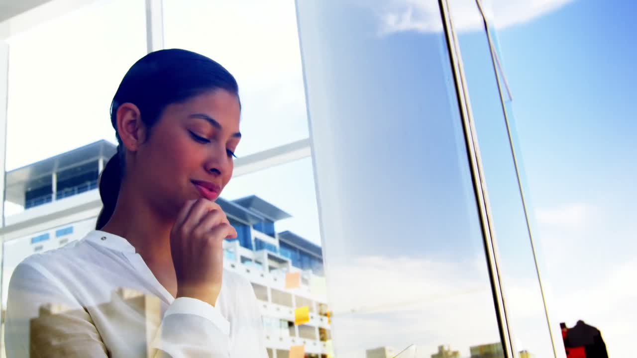 mujer mirando por la ventana de la oficina y usando un dispositivo inteligente