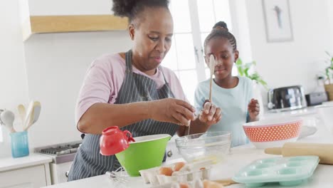 Happy-african-american-grandmother-and-granddaughter-baking-together-in-kitchen,-copy-space