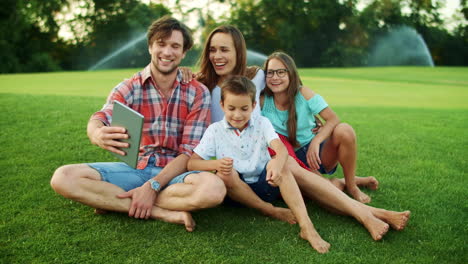 Family-laughing-together-in-park.-Family-having-video-chat-on-pad-in-meadow