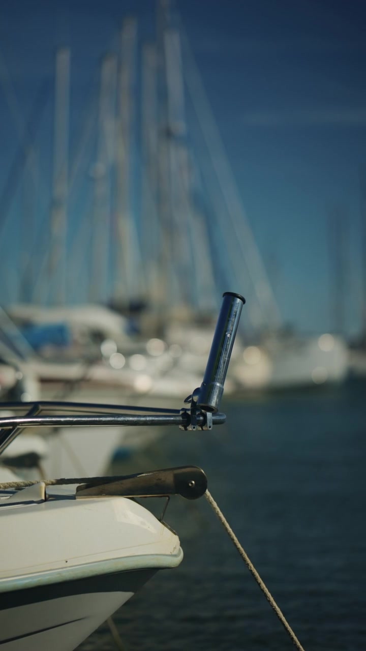 Primo piano di un portacanna da barca in metallo e di una cima d'ormeggio, con barche a vela e acqua del porto turistico sfocate che creano una scena estiva nautica.
