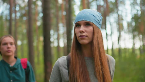 mujeres caminando a través de un bosque sereno, mujer en bandana azul y sudadera gris mirando atentamente al lado, mientras que su compañero en camisa verde está suavemente borroso detrás