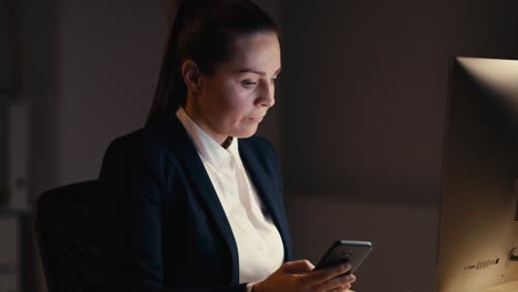 mujer de negocios adulta caucásica trabajando hasta tarde en la oficina y usando teléfono móvil