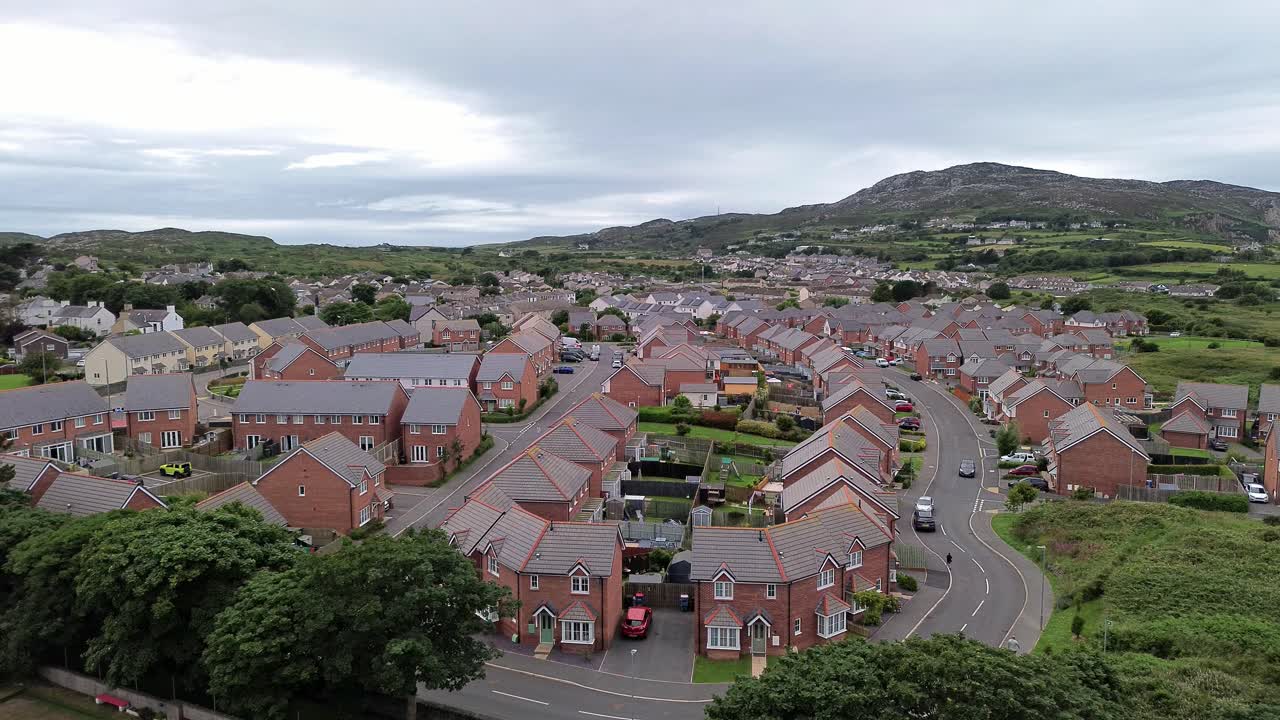 Aerial descending view of modern red brick housing neighbourhood under Holyhead mountain in Wales