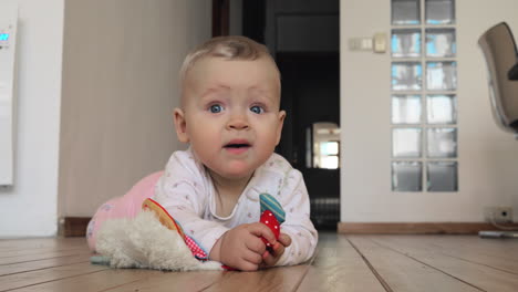 sweet blue-eyed baby girl with toy on the floor at home