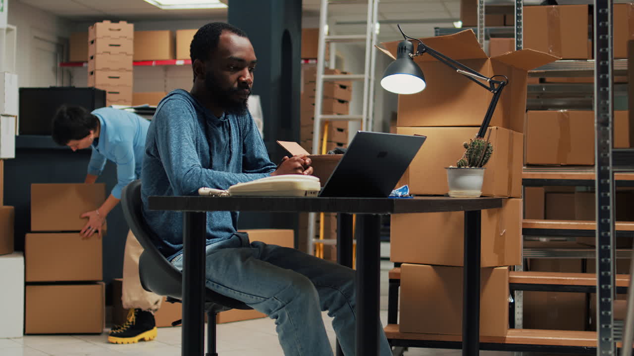 Man working on laptop surrounded by boxes in warehouse