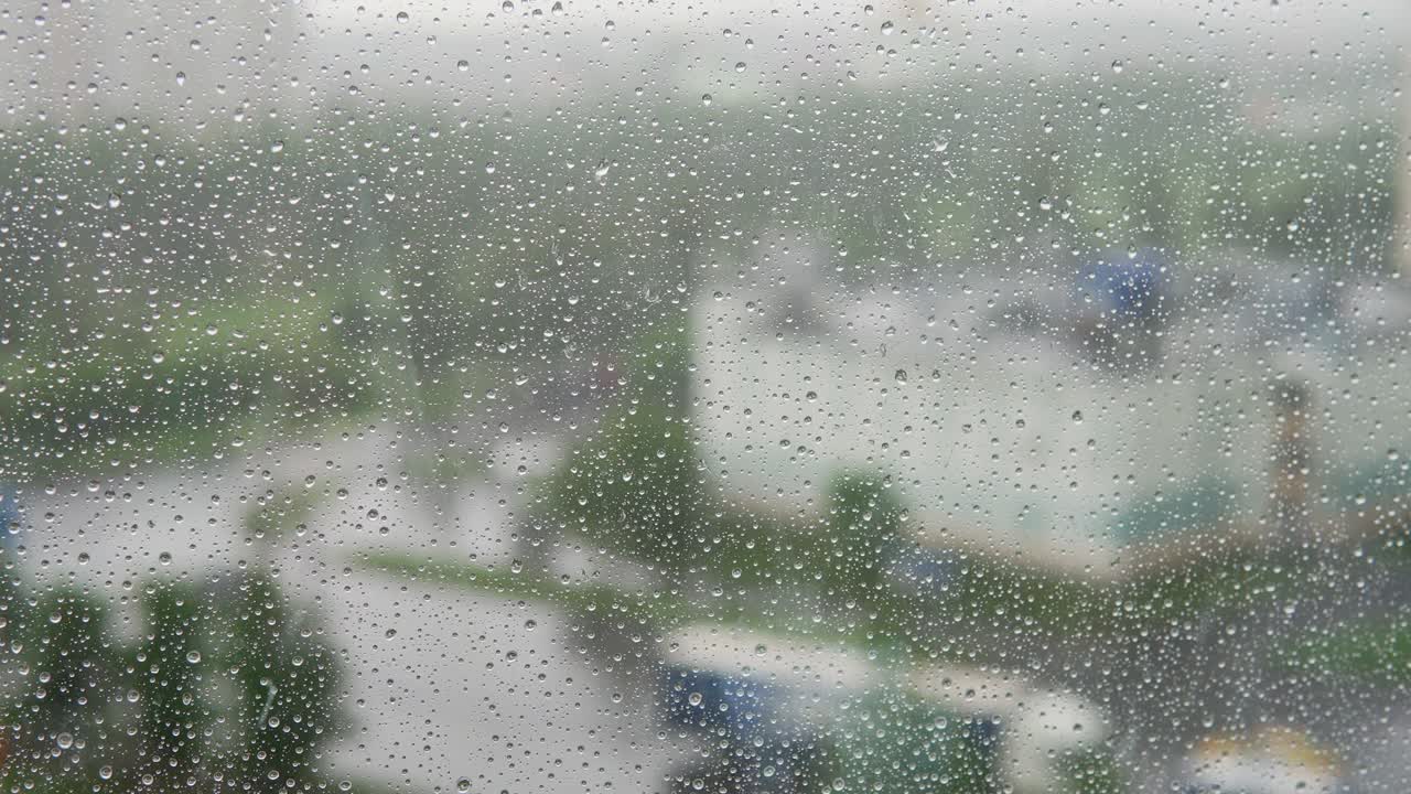 창문 표면 아래로 떨어지는 비방울. 흐릿한 배경에서 움직이는 자동차
