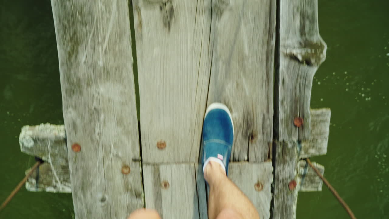 The Feet Of A Man Are Walking Along A Narrow Wooden Bridge Over A Mountain River Danger And Adventur