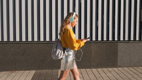 portrait of young cute attractive young girl in urban background listening to music with headphones. woman wearing yellow blouse and silver skirt