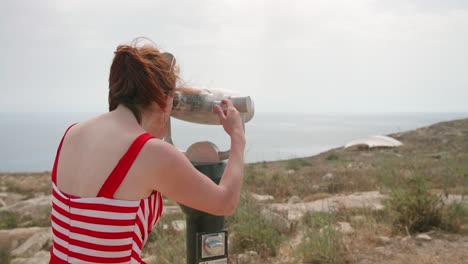 a caucasian woman looking into binoculars on a cloudy day in malta, static shot