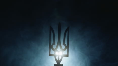 coat of arms of ukraine in the fog, illuminated by a spotlight