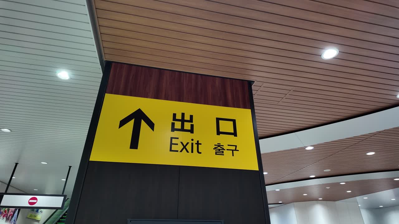 Yellow exit sign with arrow and Japanese and English words at Toyama Station, Japan, guiding people towards safety and escape route. pan left