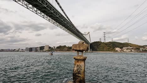 antigua linterna de roca japonesa en el agua frente al puente de kanmon y el estrecho de kanmon entre la isla japonesa de honshu y kyushu