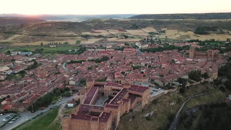 Panoramic aerial view of Sigüenza, Spain, highlighting the iconic medieval castle and the historic red-roofed town surrounded by rolling landscapes, fields, and charming architectural landmarks