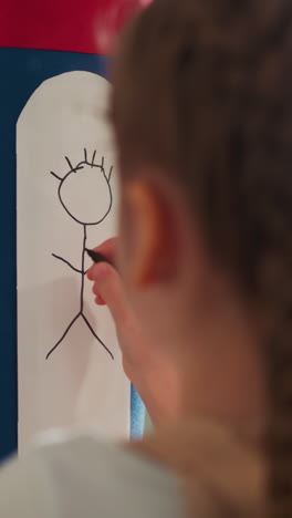 little girl with plaits draws human figure on paper glued to boxing bag close rare view. schoolgirl wants to revenge to offender in sports gym