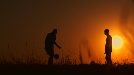 dos niños jugando al fútbol al atardecer. silueta de niños jugando con una pelota al atardezer. el concepto de una familia feliz.