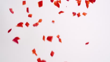 Diced-cut-red-bell-pepper-vegetable-chunks-raining-down-on-white-backdrop-in-slow-motion