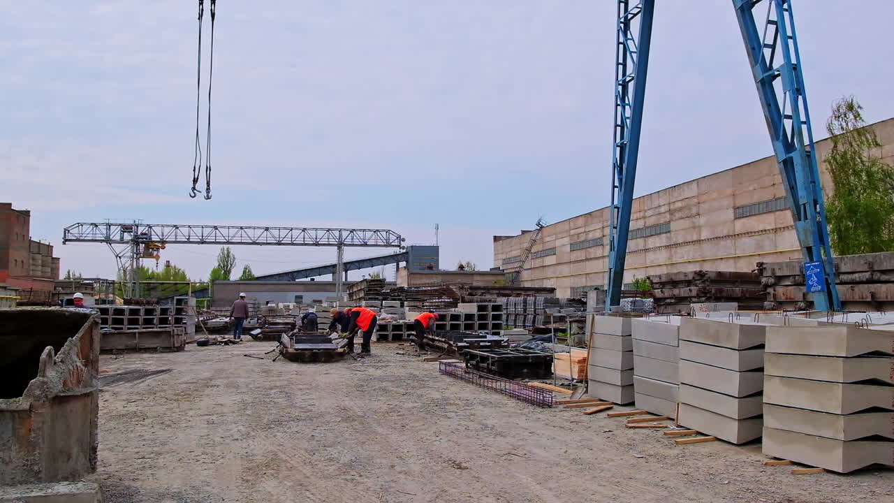 Blue crane towering over construction site. Some builders walking around the area with ferroconcrete blocks.