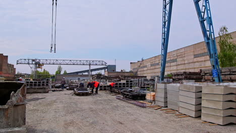 blue crane towering over construction site. some builders walking around the area with ferroconcrete blocks.