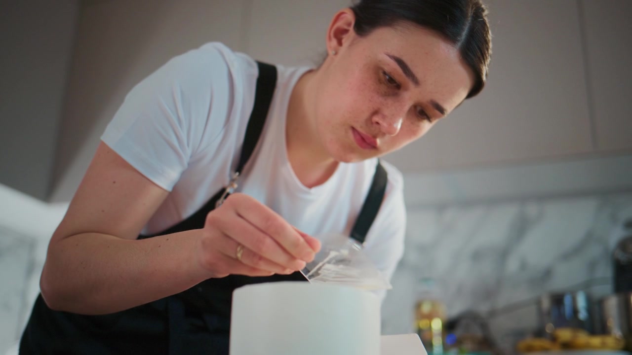 Jovem mulher concentra-se cuidadosamente enquanto decora um bolo. Ela usa um utensílio delicado para adicionar detalhes. Sua expressão demonstra concentração e precisão. Perfeito para publicidade de confeitaria, design de bolos.