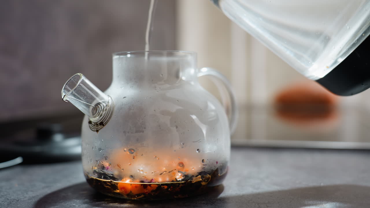 Preparing Fresh Glass Teapot By Adding Boiling Water To Loose Tea Leaves, Hastening Tea Infusion By Pouring Heated Water Over Loose Leaves In Clear Glass Teapot With Gentle Steam Rising