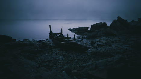 forgotten boat rests on a rocky shore under the twilight sky