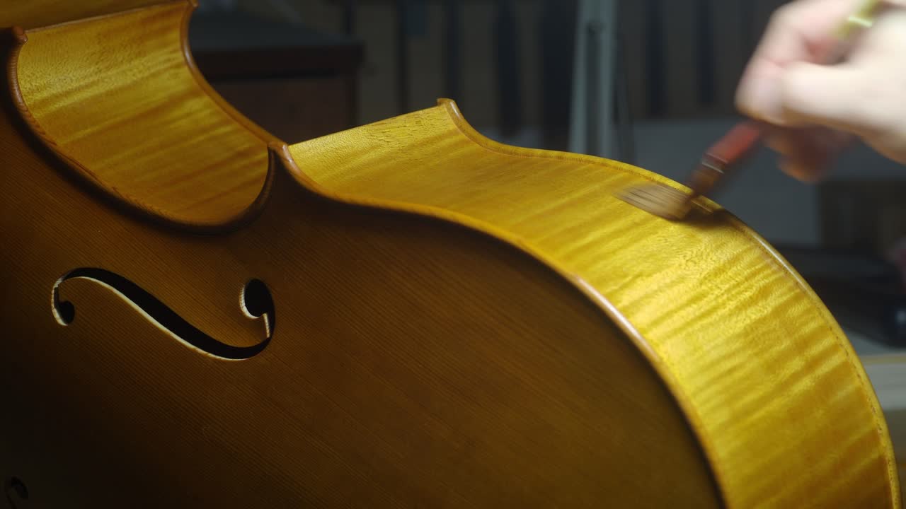 Skilled craftsman applying varnish on wooden cello smarbled ribs, highlighting delicate woodworking techniques in instrument making process