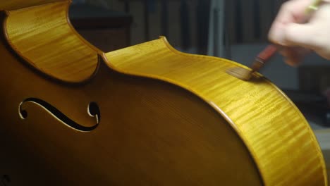 skilled craftsman applying varnish on wooden cello smarbled ribs, highlighting delicate woodworking techniques in instrument making process