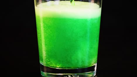a bright green liquid is poured into a glass, creating a foamy, effervescent surface.