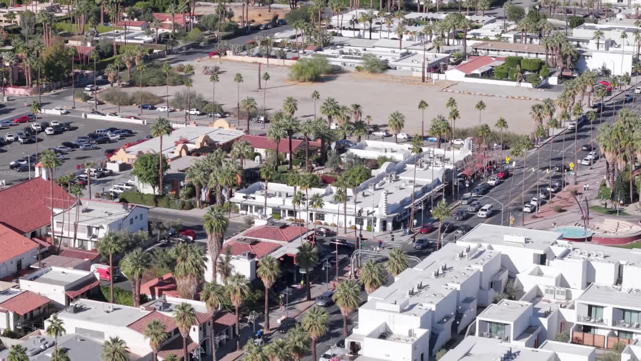 Downtown area of Palm Springs, California lined with palm trees on a sunny day - aerial flyover