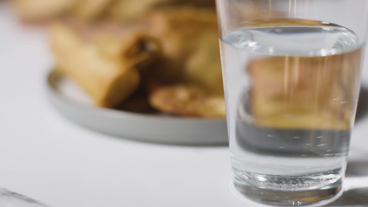 primer plano de un plato de samosas y un vaso de agua sobre una superficie de mármol celebrando el festival musulmán del eid