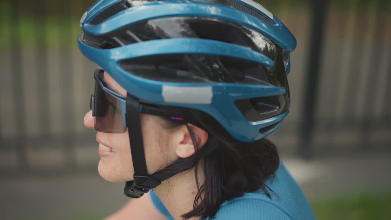 woman cyclist wearing blue helmet profile. close side shots of adult woman on bicycle with sunglasses and chinstrap fastened textured blue aerodynamic helmet with ventilation channels and subtle