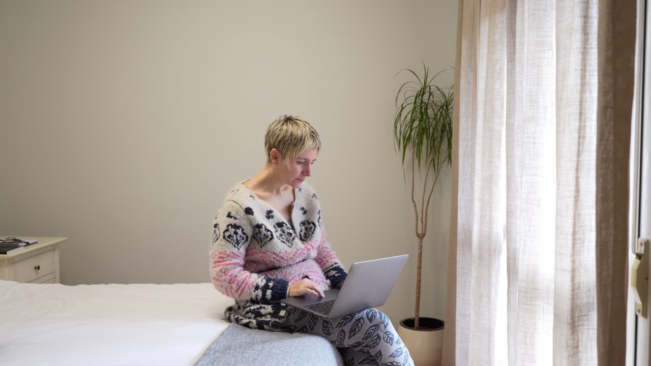 Kvinde arbejder på bærbar computer i soveværelset