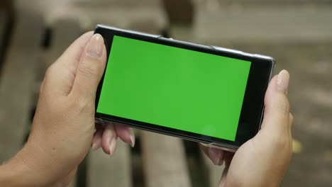 mujer rubia con un teléfono inteligente de pantalla verde al aire libre