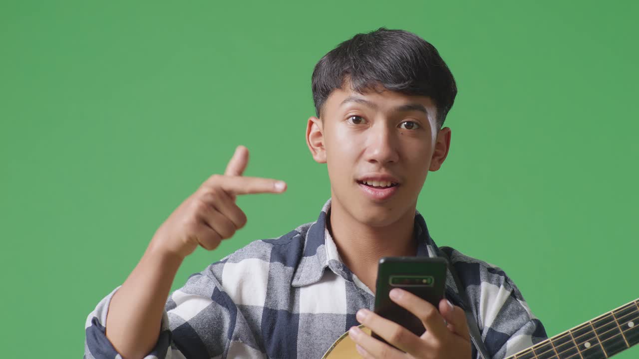 초록색 화면 배경에서 손에 스마트폰을 가리키는 기타를 들고 있는 아시아 십대