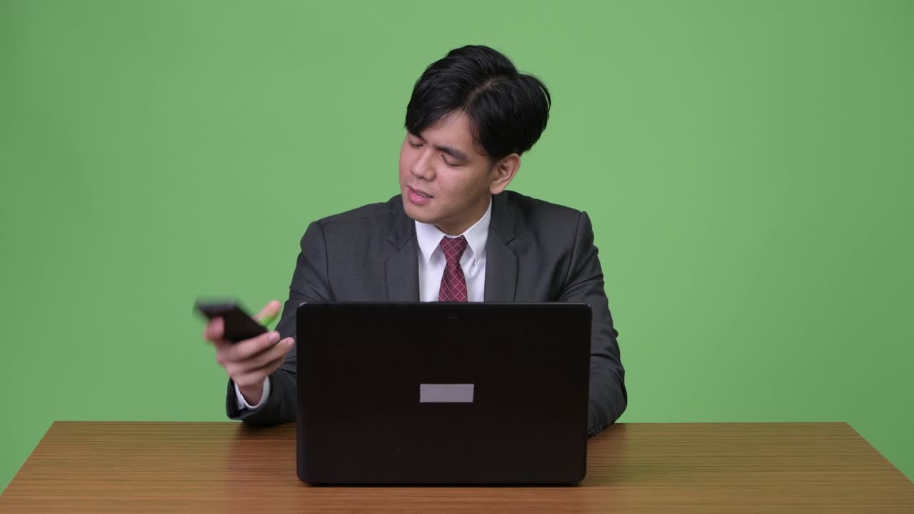 젊은 잘생긴 아시아 사업가가 초록색 배경에 노트북을 가지고 일하고 있습니다.