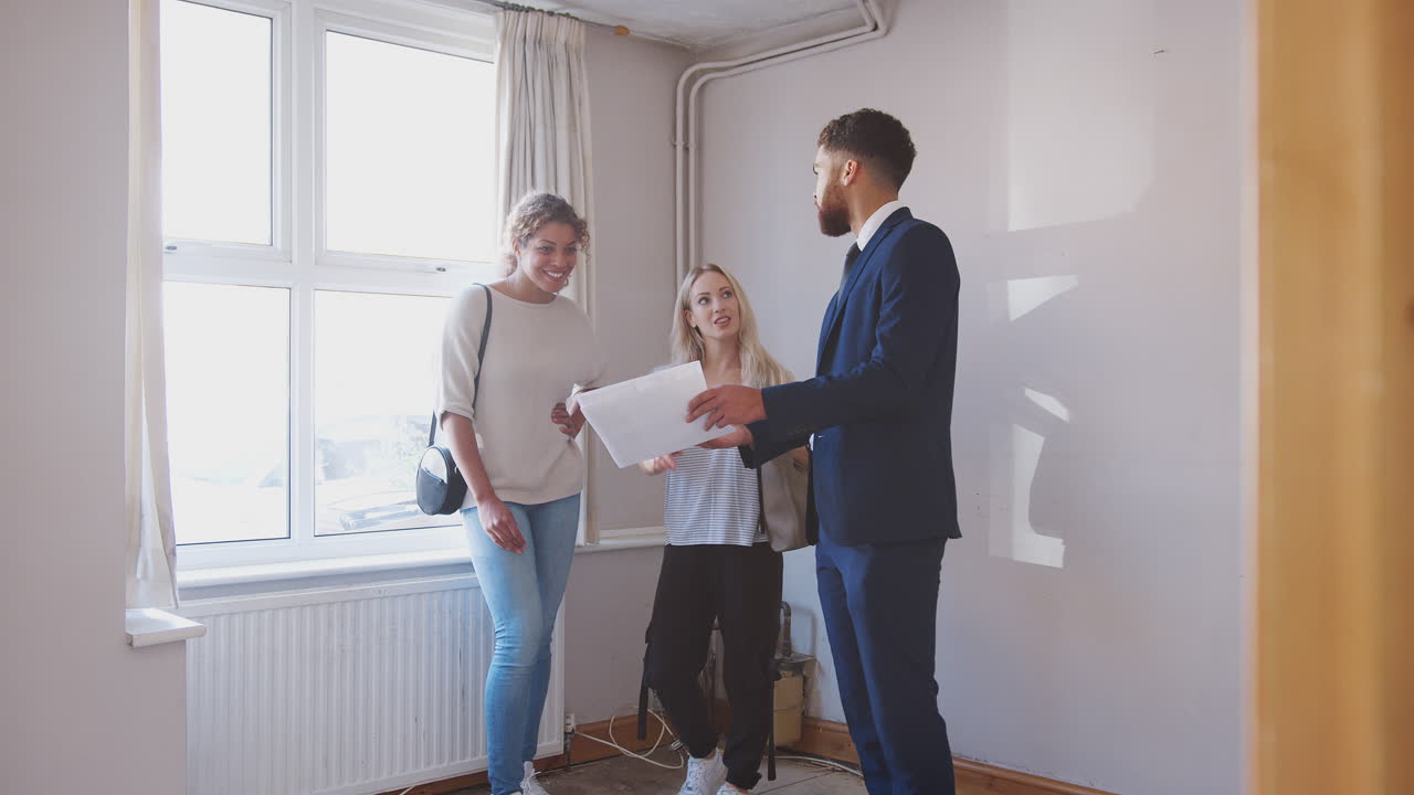 Two Female Friends Buying House For First Time Looking At House Survey With Realtor