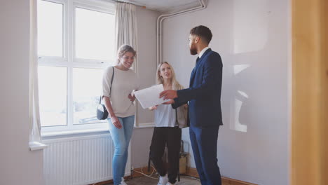 Dos-Amigas-Comprando-Una-Casa-Por-Primera-Vez-Mirando-La-Encuesta-De-La-Casa-Con-Un-Agente-Inmobiliario