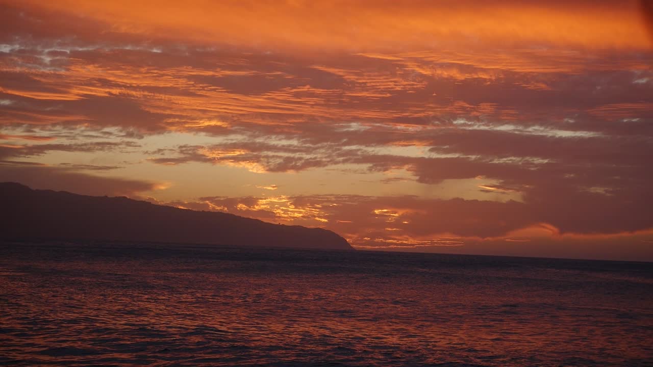 A stunning sunset over Oahu Hawaii North Shore Kaena Point in orange and purple with rolling waves