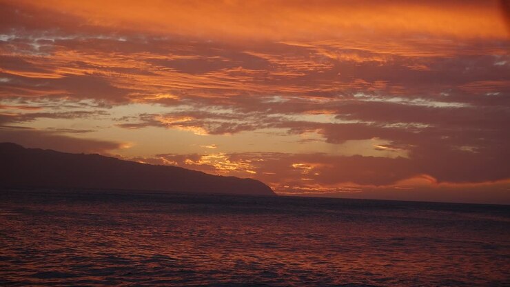 A stunning sunset over Oahu Hawaii North Shore Kaena Point in orange and purple with rolling waves