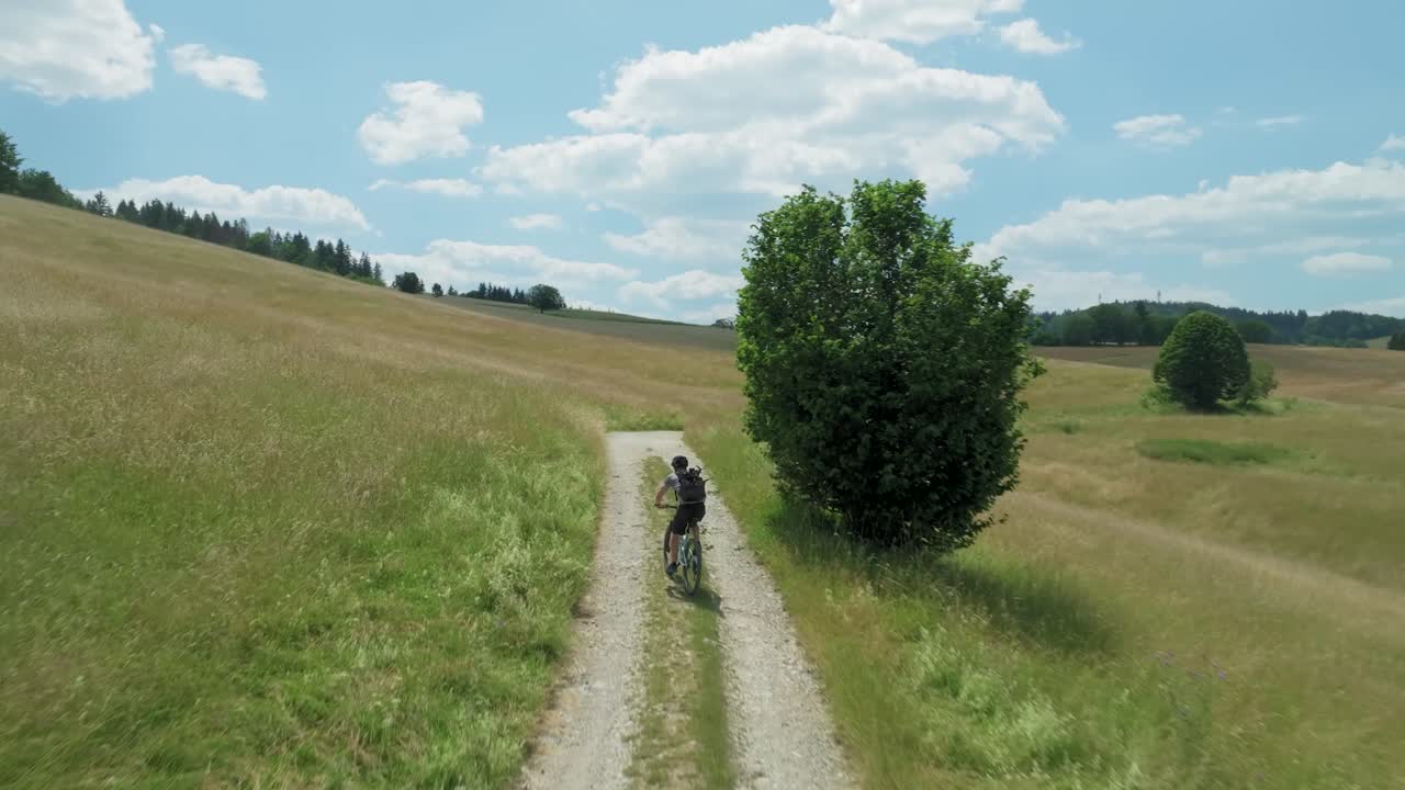 Aerial footage of a drone following a mountain biker riding on a nice unpaved cycling path on a warm summer evening with an iddylic sunset