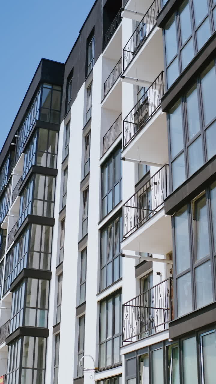 Modern facade of multi-storied-building. New apartment building in black and white colors against blue sky. Drone view. Vertical video