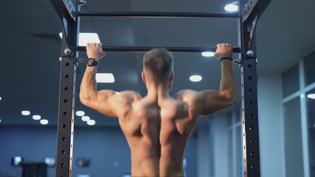 Handsome strong athletic man pumping up back muscles. Fitness man doing pull-ups exercises on a crossbar in gym naked torso. Workout fitness and bodybuilding concept. Rear view.