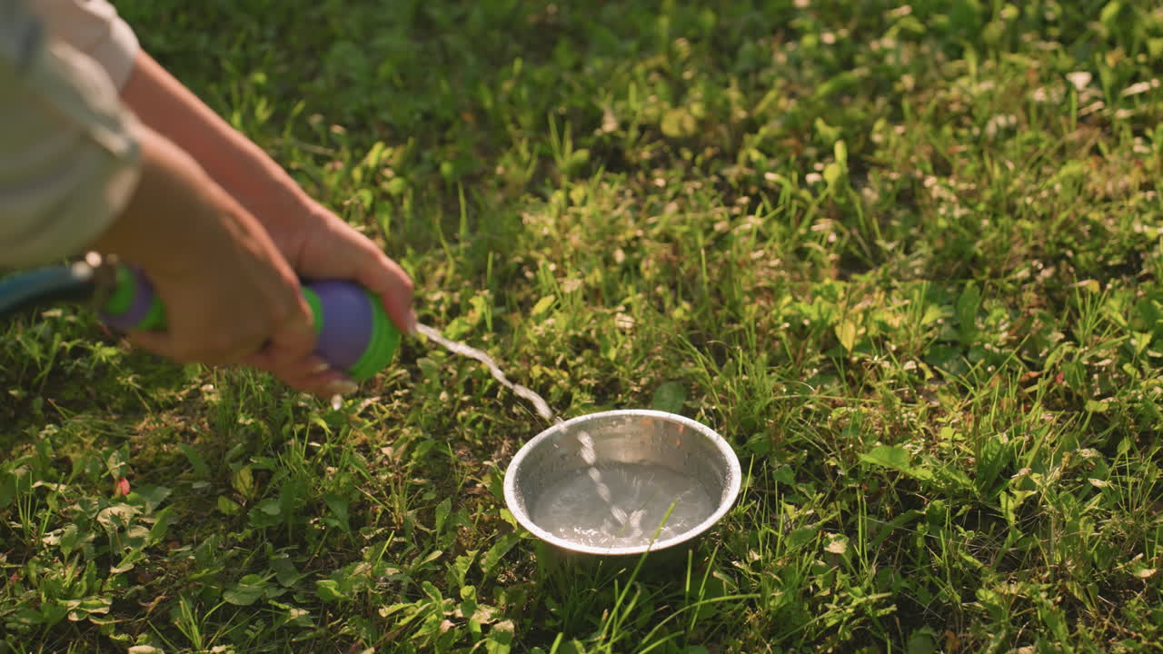 잔디에서 호스에서 금속 그에 물을 부는 사람의 클로즈업, 은 빛이 배경에서 반사를 만니다.