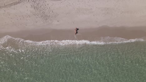 Aerial:-Young-woman-in-bikini-on-sandy-beach-waves-at-ascending-camera