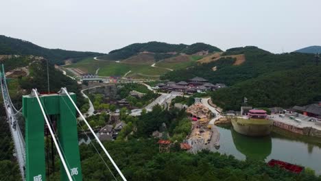 Dynamic-cinematic-aerial-sliding-left-view-revealing-tourists-on-suspension-glass-bridge-at-Huaxiacheng-theme-park-in-Weihai-China