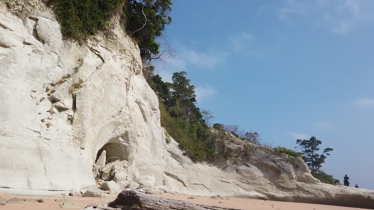 샷은 흰색 백악질 절벽에서 후미가 있는 황금빛 모래로 내려가고 멀리 있는 두 사람이 산호 위로 걸어가려고 합니다.