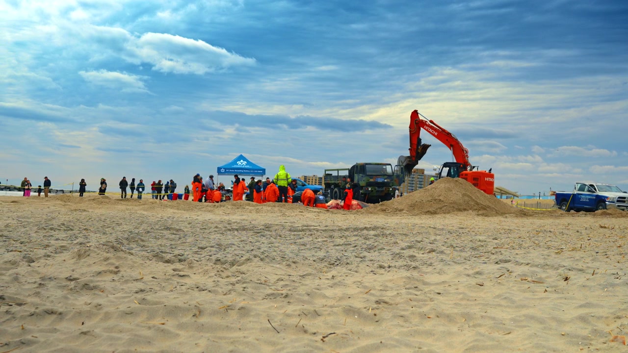 New York, USA, 1 aprile 2026: Ampia vista di un intervento per spiaggiamento di mammiferi marini sulla spiaggia. Operazione su larga scala con scienziati e macchinari pesanti che gestiscono una balena deceduta sotto un cielo nuvoloso.