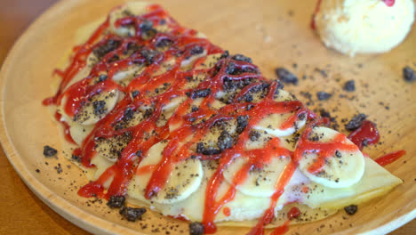 crepe-with-banana,-whipped-cream-and-strawberry-sauce-on-wood-plate