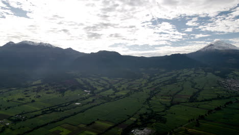 Backwards-drone-shot-showing-the-snowy-top-of-the-popocatepetl-and-iztaccihutal-volcanoes-in-mexico-city-and-the-lush-forests-that-surround-it